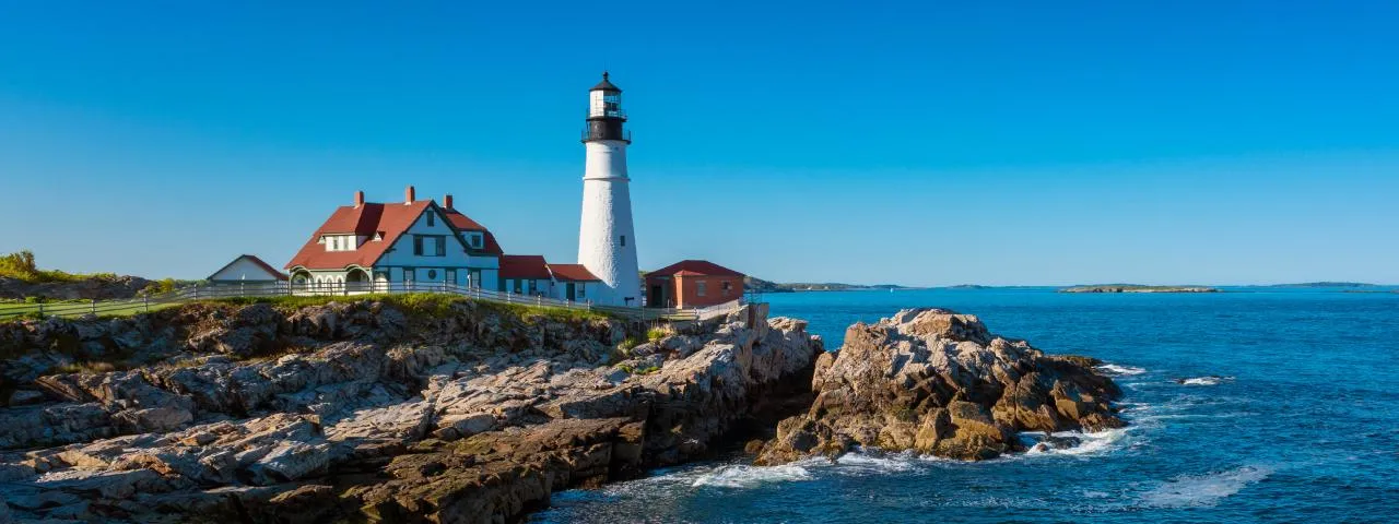 Portland Head Light, a white lighthouse and red-roofed keeper's house on a rocky Maine headland under a clear sky